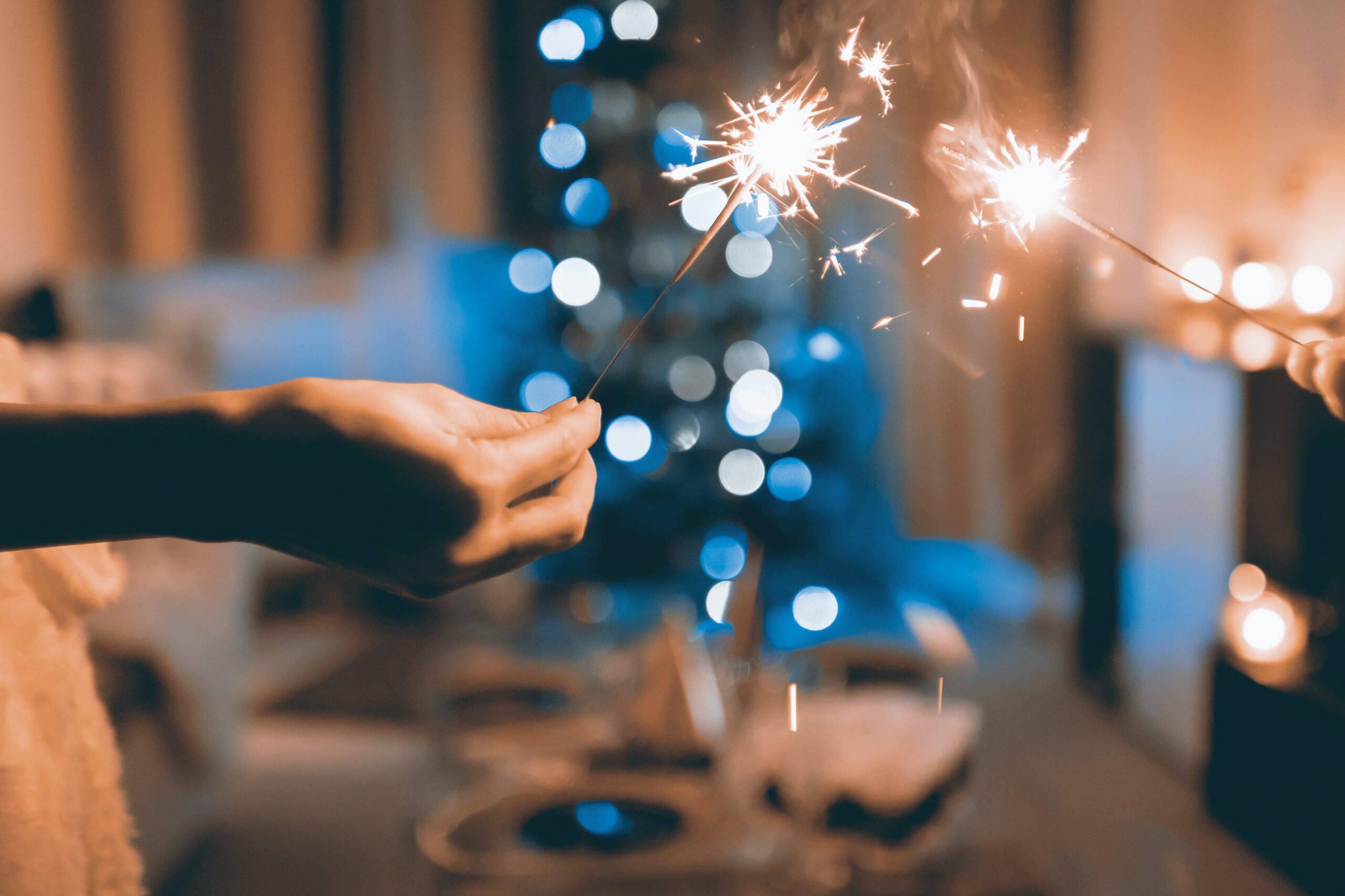 A person holding a sparkler in front of a Christmas tree.